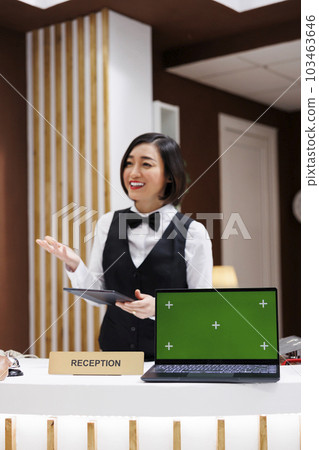 Hotel worker with green screen on desk, welcoming people and working on registration with tablet. Asian receptionist having laptop with chroma key display and isolated mockup screen. Hotel worker with green screen on desk, welcoming people and working on registration with tablet. Asian receptionist having laptop with chroma key display and isolated mockup screen. 103463646