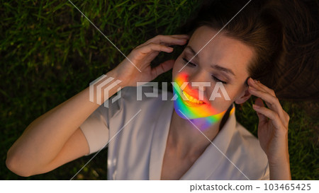 Top view of caucasian woman with rainbow ray on her face lies on green grass. Top view of caucasian woman with rainbow ray on her face lies on green grass. 103465425