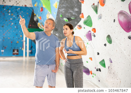 Young woman discussing climbing options with an older man at climbing wall 103467847