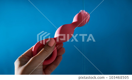 Woman pouring lubricant on pink anal beads on blue background. Woman pouring lubricant on pink anal beads on blue background. 103468505