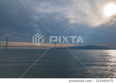 A photograph of the Akashi Kaikyo Bridge, Awaji Island and the Seto Inland Sea in the evening. The sunlight reflects off the surface of the sea, creating a magical atmosphere. 103469470
