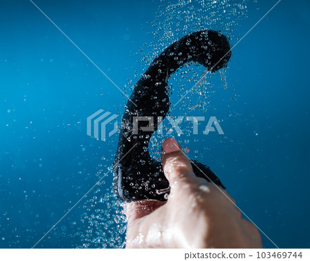 A woman washes a black prostate stimulator under running water on a blue background. Sex toy hygiene concept. A woman washes a black prostate stimulator under running water on a blue background. Sex toy hygiene concept. 103469744
