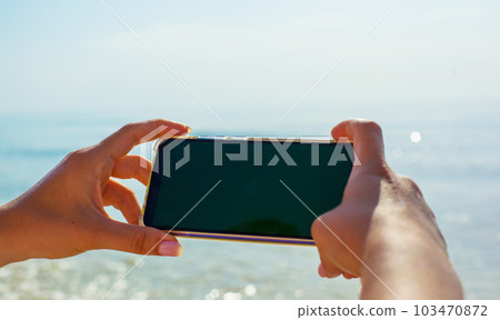 Close up photo of girls hands holding phone against the sea background Close up photo of girls hands holding phone against the sea background 103470872