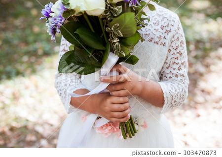 Hands of little girl holding bouquet with white silk ribbon Hands of little girl holding bouquet with white silk ribbon 103470873