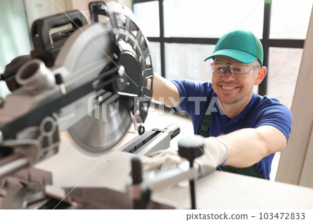Carpenter with goggles cuts boards with sawing machine 103472833