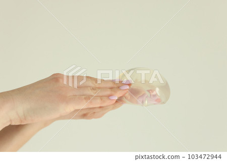 Woman hands hold silicone breast implant on light background Woman hands hold silicone breast implant on light background 103472944
