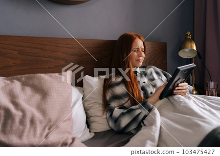 Side view of grief-stricken young woman lying on bed holding photo in frame and crying closed eyes, touching picture with love at home. Concept of nostalgia, grief, longing and loneliness. 103475427
