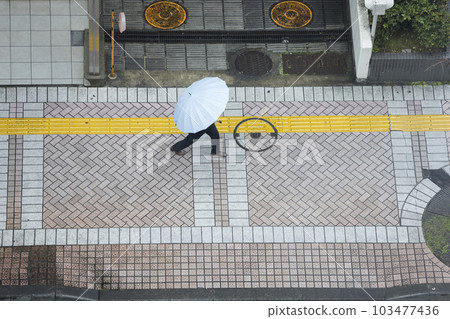 一個商人在雨中打著傘走在人行道上 103477436