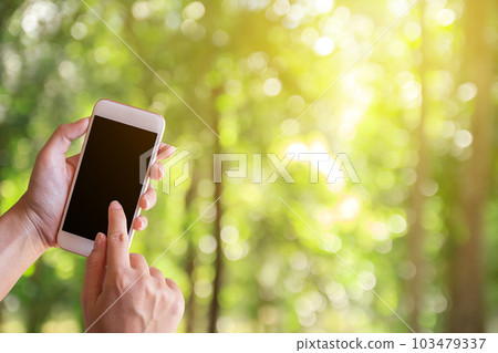 Women hand shows mobile smartphone in vertical position with blurred green bokeh background Women hand shows mobile smartphone in vertical position with blurred green bokeh background 103479337