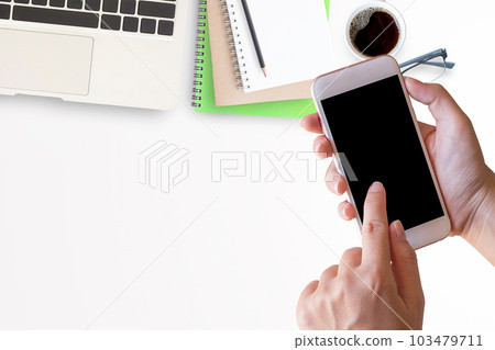 Smart phone in female hand with office desk with laptop Smart phone in female hand with office desk with laptop 103479711