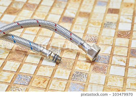 Plumbing. Flexible metal stainless steel faucet hoses on light brown pvc panel Plumbing. Flexible metal stainless steel faucet hoses on light brown pvc panel 103479970