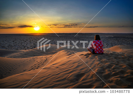 Woman watching a sunset over the sand dunes of the Arabian Desert in Oman 103480778