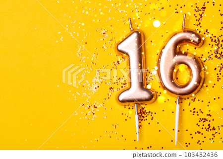 Gold candles in the form of number sixteen on yellow background with confetti. 16 years celebration. Gold candles in the form of number sixteen on yellow background with confetti. 16 years celebration. 103482436