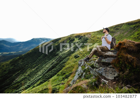 Man on top of a mountain sitting on a rock Man on top of a mountain sitting on a rock 103482877