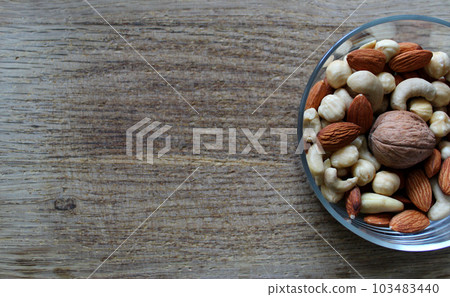 Bowl With Peeled Almonds, Cashew And Hazelnuts And Whole Walnut On A Wooden Board At Side Of Image 103483440