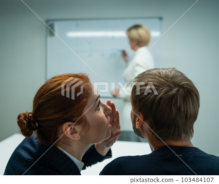 Caucasian woman blonde leads the presentation. Colleagues gossip behind the boss's back. Caucasian woman blonde leads the presentation. Colleagues gossip behind the boss's back. 103484107