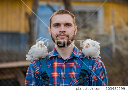 A farmer of European Caucasian a man with a beard portrait in a shirt with two dwarf white chickens on his shoulder, close-up against the backdrop of the countryside A farmer of European Caucasian a man with a beard portrait in a shirt with two dwarf white chickens on his shoulder, close-up against the backdrop of the countryside 103489299