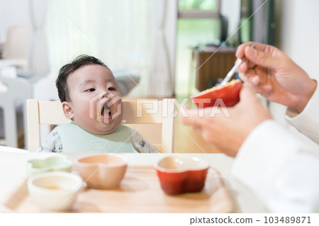 一個8個月大的嬰兒張著嘴等著讓爸爸吃嬰兒食品 一個8個月大的嬰兒張著嘴等著讓爸爸吃嬰兒食品 103489871