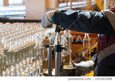 Glassworks. Glass industry. Working hands hold a glass bottle on the background of a conveyor belt. Glassworks. Glass industry. Working hands hold a glass bottle on the background of a conveyor belt. 103492906