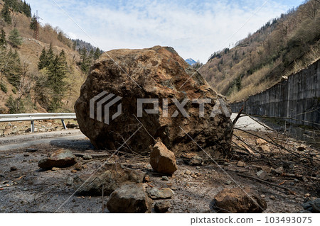 A huge rock fell from the mountains onto the road, destroying the asphalt and blocking half of the roadway. A huge rock fell from the mountains onto the road, destroying the asphalt and blocking half of the roadway. 103493075