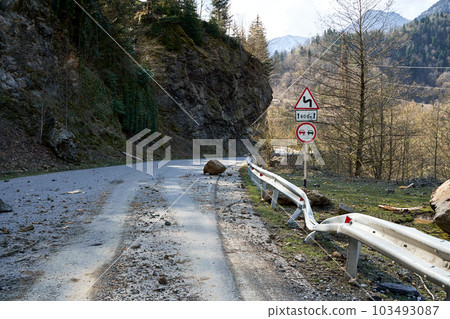 A huge rock fell from the mountains onto the road, destroying the asphalt and blocking half of the roadway. A huge rock fell from the mountains onto the road, destroying the asphalt and blocking half of the roadway. 103493087