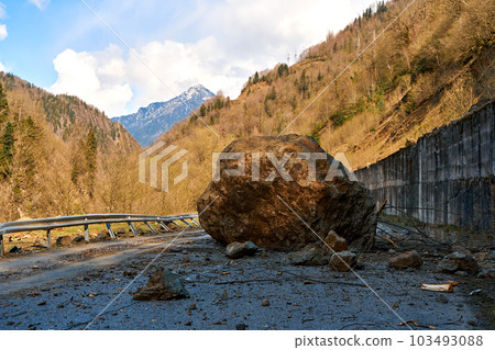 A huge rock fell from the mountains onto the road, destroying the asphalt and blocking half of the roadway. 103493088