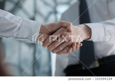 Two businessmen shake hands on the background of empty modern office, signing of a contract concept, close up Two businessmen shake hands on the background of empty modern office, signing of a contract concept, close up 103494184