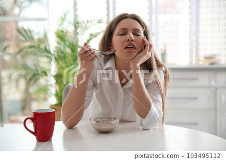 Sleepy young woman eating breakfast at home in morning 103495112