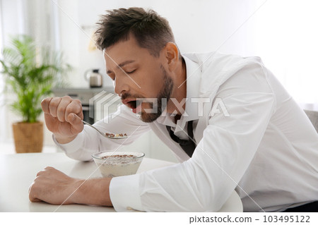 Sleepy man eating breakfast at home in morning 103495122