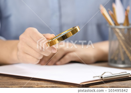 Woman using magnifying glass at table, closeup Woman using magnifying glass at table, closeup 103495842