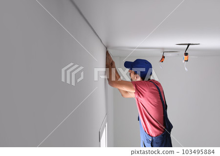 Worker installing stretch ceiling in empty room 103495884