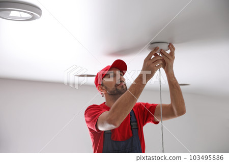 Worker repairing lamp on stretch ceiling indoors 103495886