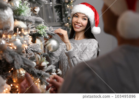 Happy young couple decorating Christmas tree together at home 103495896