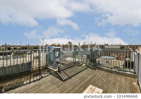 an outdoor area with wooden flooring and metal railings on the top of a building, under a blue sky filled with white 103496666
