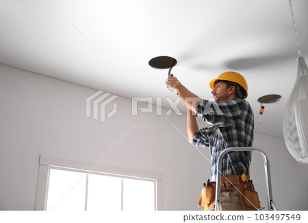 Worker installing lamp on stretch ceiling indoors. Space for text 103497549