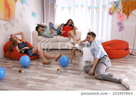 Friends suffering from hangover in messy room after party 103497663