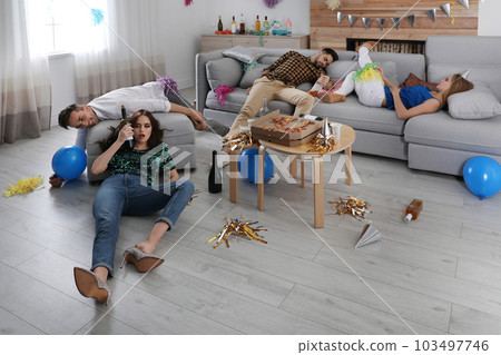 Drunk friends suffering from hangover in messy room after party Drunk friends suffering from hangover in messy room after party 103497746
