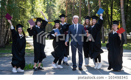 A university professor and seven robed graduates are jumping outdoors. 103498341