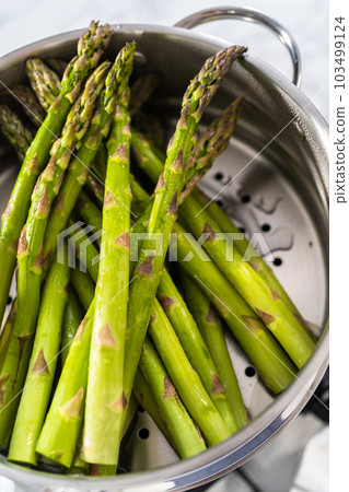 Steaming fresh asparagus in stainless steel steaming pot. 103499124