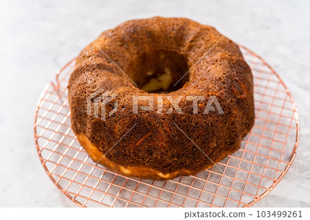 Removing freshly baked carrot bundt cake from the bundt cake pan to round the cooling rack. 103499261