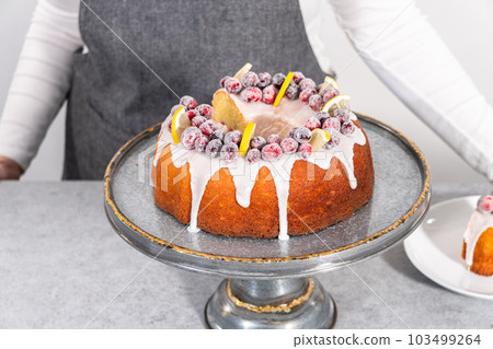 Sliced lemon cranberry bundt cake decorated with sugar cranberries and lemon wedges on a cake stand. 103499264