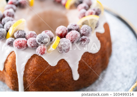 Lemon cranberry bundt cake decorated with sugar cranberries and lemon wedges on a cake stand. 103499314