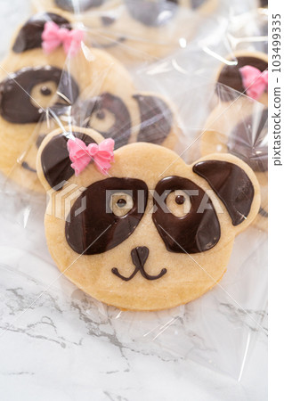 Packaging panda-shaped shortbread cookies with chocolate icing into individual clear bags. Packaging panda-shaped shortbread cookies with chocolate icing into individual clear bags. 103499335