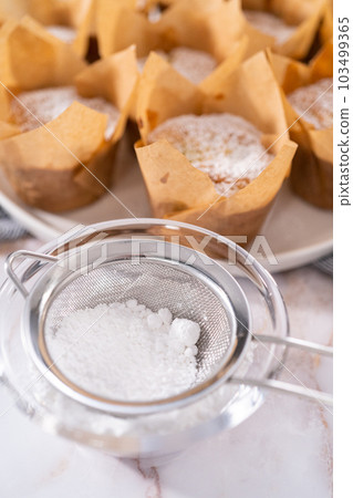Garnishing freshly baked apple sharlotka muffin dusted with powdered sugar. 103499365