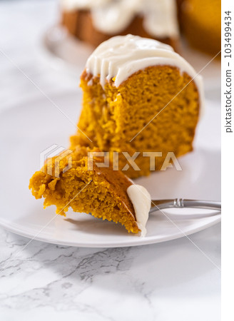 Slice of homemade pumpkin bunt cake with cream cheese frosting on a white plate. 103499434