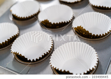 Scooping cupcake batter with dough scoop into a baking cupcake pan with liners to bake dulce de leche cupcakes. 103499445