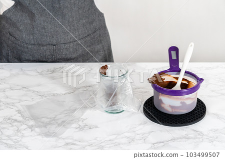 Transferring melted chocolate into piping bags for icing panda-shaped shortbread cookies. Transferring melted chocolate into piping bags for icing panda-shaped shortbread cookies. 103499507