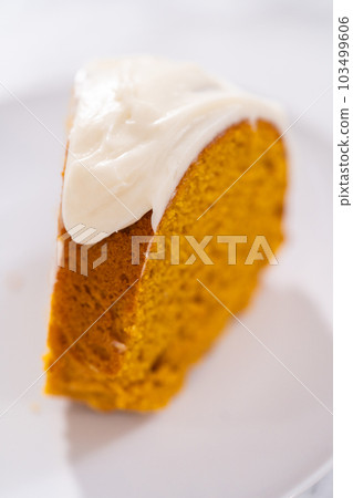 Slice of homemade pumpkin bunt cake with cream cheese frosting on a white plate. 103499606
