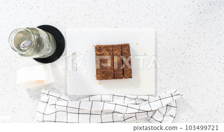Flat lay. Cutting chocolate peanut butter fudge into small pieces on a white cutting board. 103499721