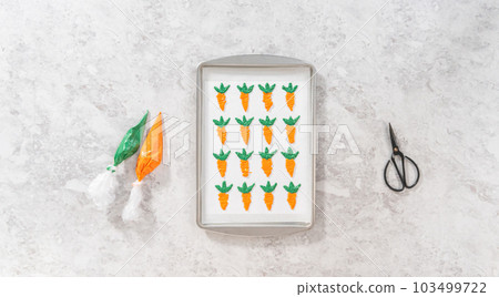 Flat lay. Piping melted chocolate from a piping bag over the parchment paper to make chocolate carrot cake toppers. 103499722